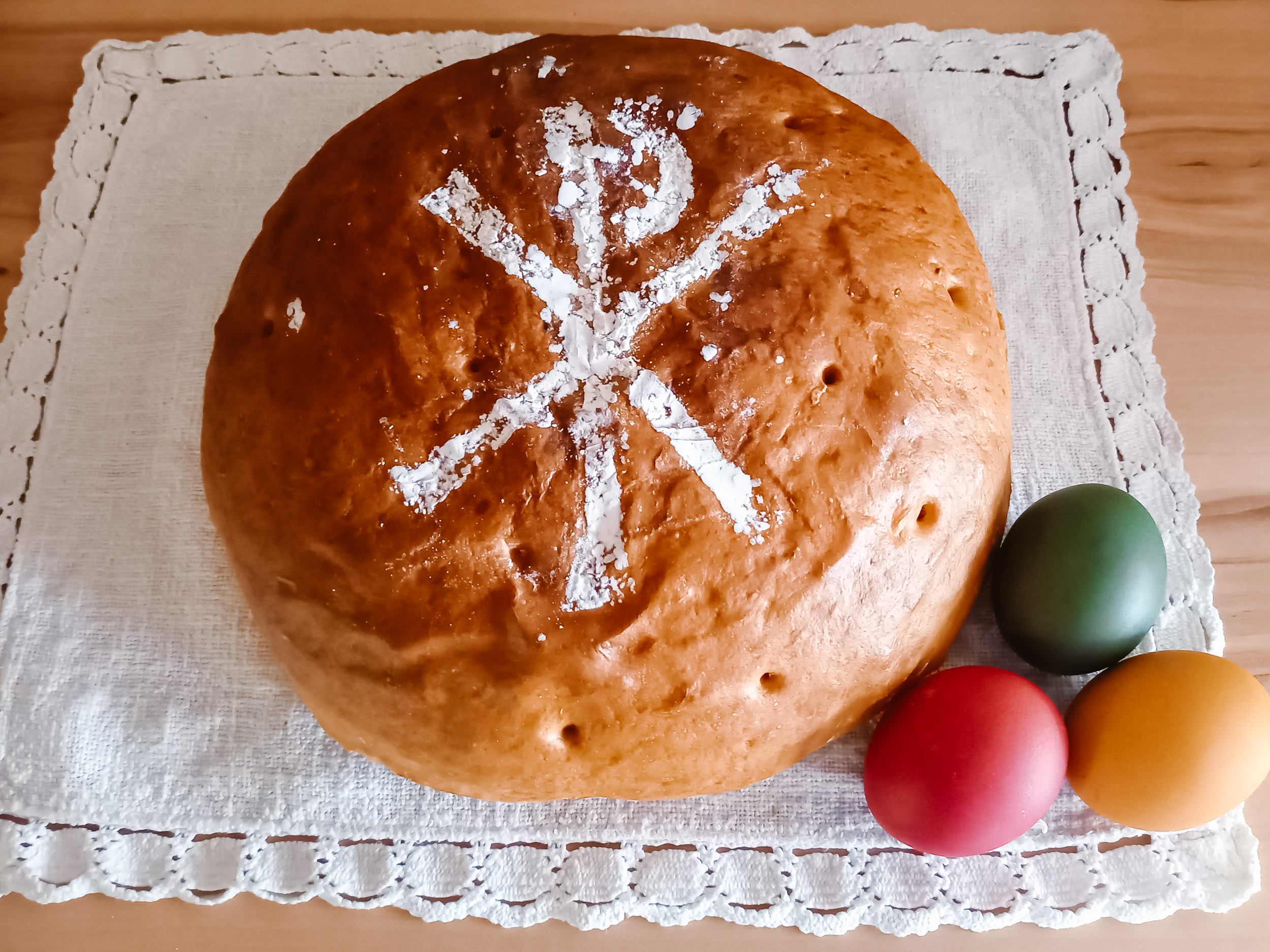Osterbrot liegt auf einem weißen Tuch, daneben je ein rotes, grünes und gelbes Ei.
