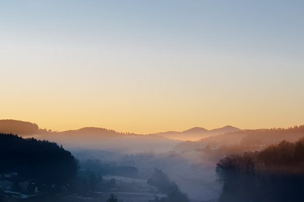 Sonnenaufgang zum Jahreswechsel, Nebel hängt im Tal, Sonnestrahlen tauchen Gleichenberger Kogel in warmes Licht