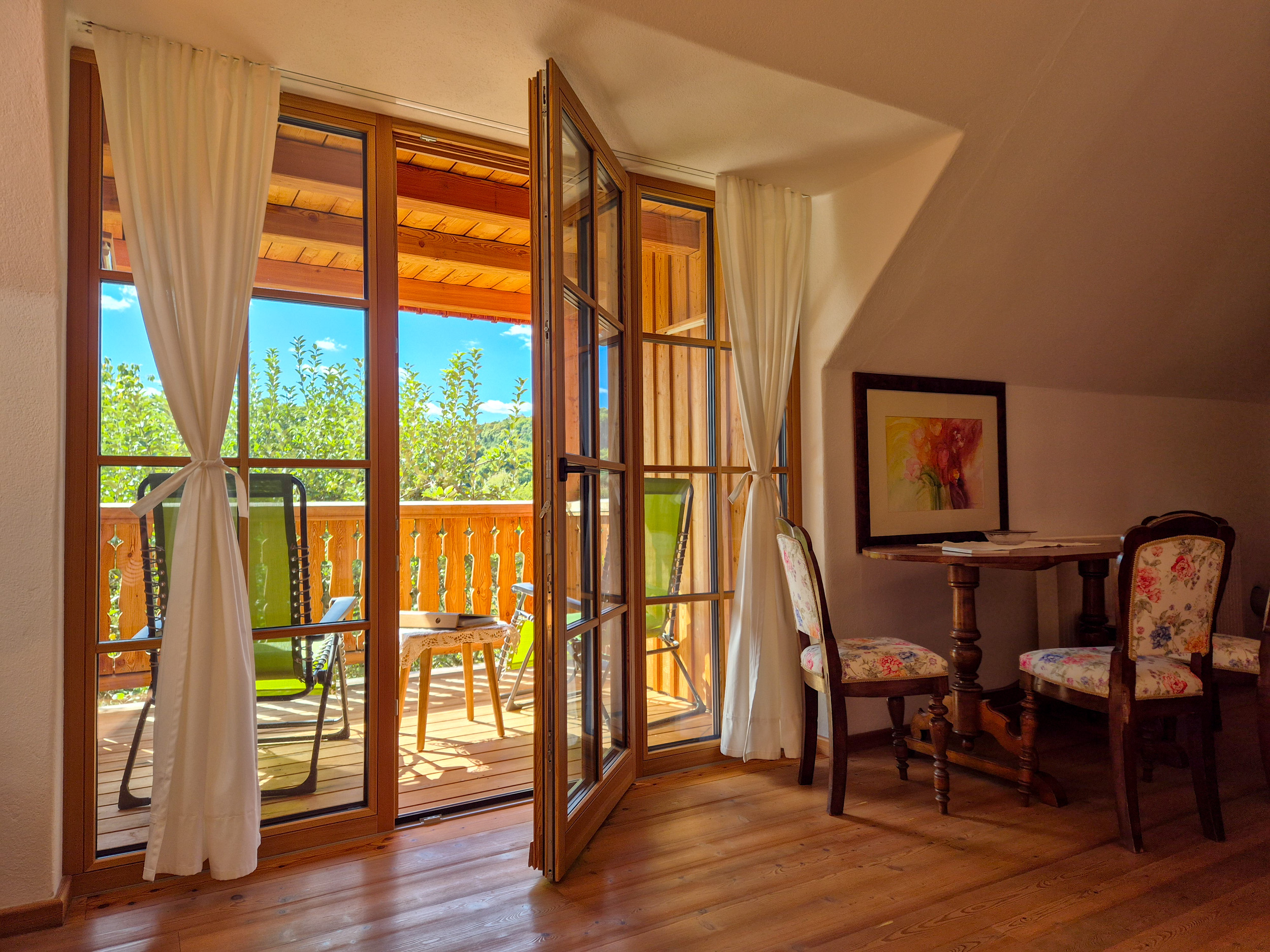 Double room Durch ein halb geöffnete Balkontür Blick auf die Veranda mit grünen Liegestühlen