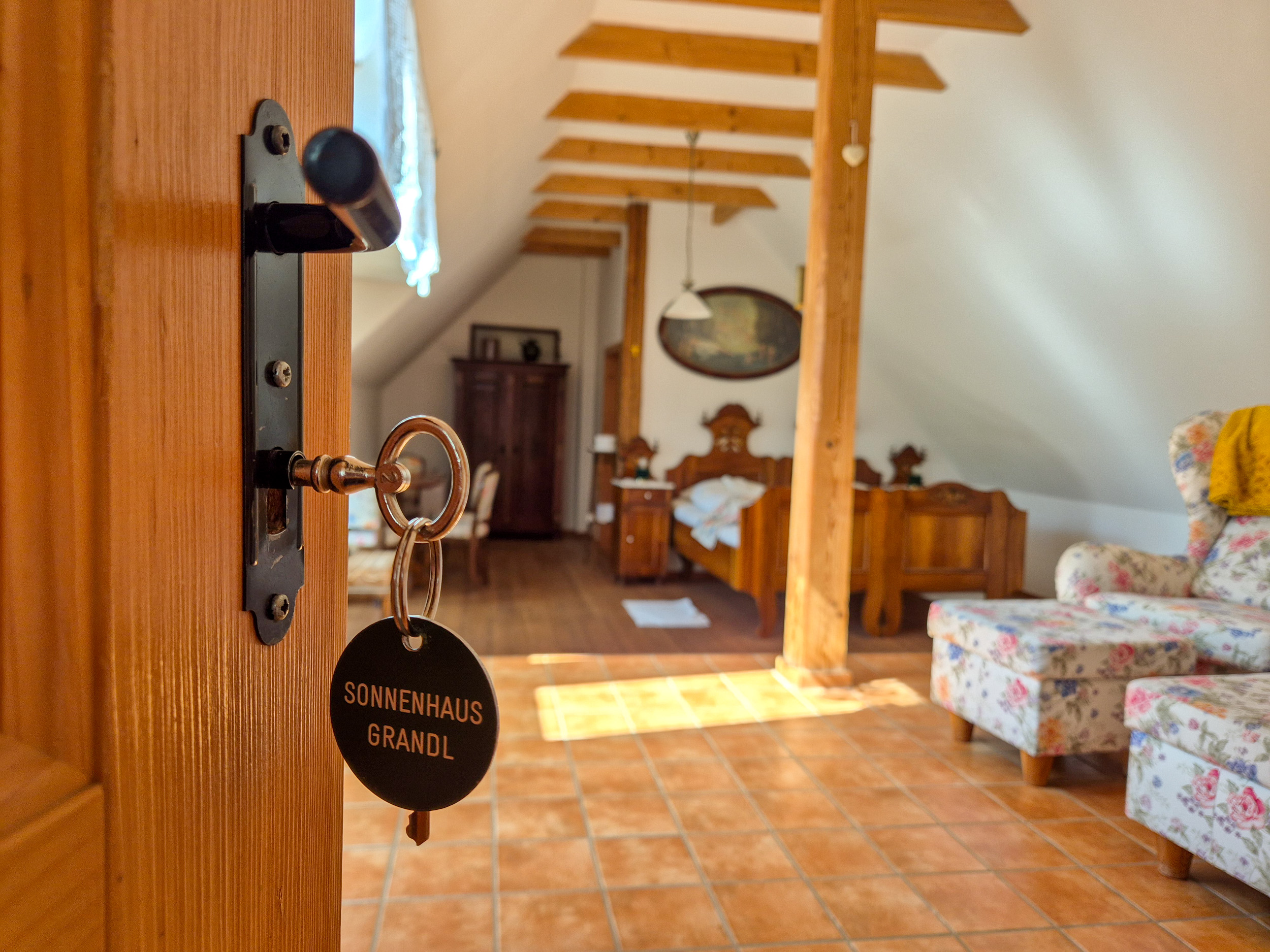 Eine Tür öffnet sich zum Zimmer am Land, im Schlüsselloch steckt ein Schlüssel mit rundem Schlüsselanhänger, der die Aufschrift Sonnenhaus Grandl trägt