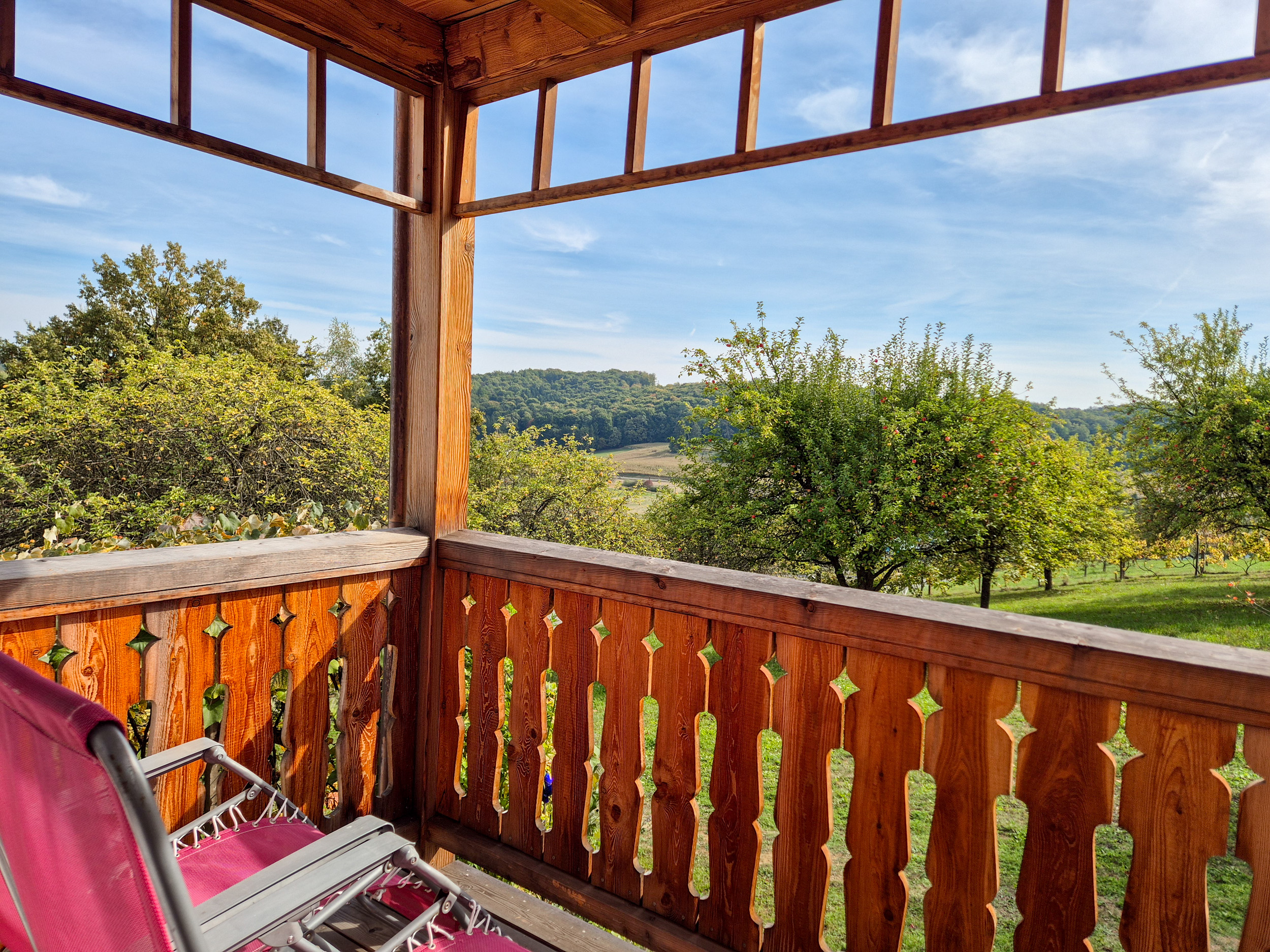 Über die Veranda mit Holzbalkon und roten Liegestühlen geht der Blick in die grünen Kronen der Apfelbäume